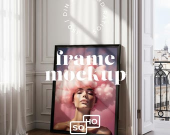 May include: A black framed art print leaning against a white wall. The print features a woman with pink cloud-like hair. The words "frame mockup" are displayed in white, along with the logo "SO MOCKUPS".