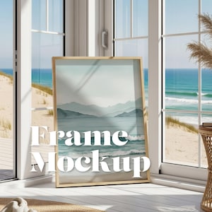 May include: A framed watercolor print featuring a coastal landscape with mountains and ocean waves. The frame is a light wood color. The words "Frame Mockup" are displayed in white text on the bottom of the frame.
