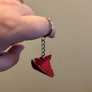 Puede incluir: Un llavero de metal rojo con forma de triángulo con una cadena y un anillo plateados.
