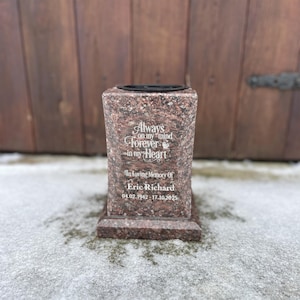 May include: A red granite memorial vase with a black top. The vase has the inscription "Always on my mind, Forever in my Heart" and "In Loving Memory Of Eric Richard 04.02.1942-17.10.2025".