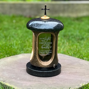 Peut inclure: Une lanterne funéraire en granit noir surmontée d'une croix dorée. Le panneau en verre porte l'inscription gravée : YOUR LIGHT WILL FOREVER SHINE IN OUR HEARTS, IN LOVING MEMORY OF DAVID WILSON, 1964-2024. La base et le couvercle sont noirs polis.