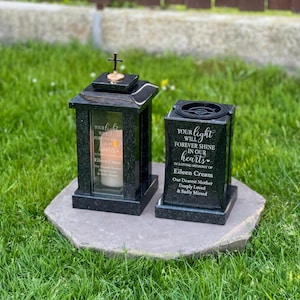 Op de afbeelding: Een zwarte granieten graflantaarn met een klein kruisje bovenop en een bijpassende zwarte granieten grafvaas. Beide objecten zijn voorzien van een witte inscriptie: Your light will forever shine in our hearts, in loving memory of Eileen Crean.