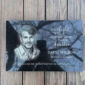 Könnte beinhalten: Schwarze Granit-Gedenktafel mit einem Porträt eines Mannes und der Inschrift "Your light will forever shine in our hearts". Die Tafel enthält den Namen David Wilson und die Daten 10.07.1950 - 24.10.2025. Der Satz "Always on my mind forever in my heart..." ist ebenfalls enthalten.