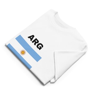 May include: White t-shirt with the Argentinian flag and the text "ARG" printed on the front.