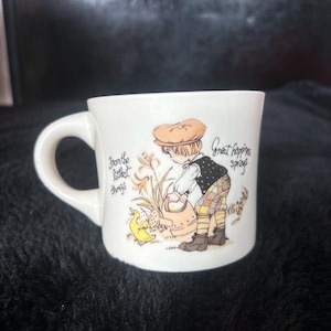 May include: White ceramic mug with a handle, featuring a vintage illustration of a young person watering a plant. The mug has the text "From the littlest things" and "Great happiness springs".