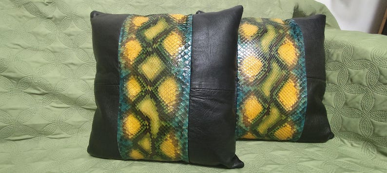 Op de afbeelding: Twee decoratieve kussens met zwart leer en een slangenhuidpatroon in groen, geel en blauw.