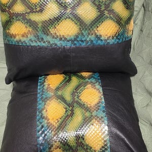 Op de afbeelding: Twee zwarte leren kussens met een geel, groen en blauw slangenhuidpatroon aan de voorkant.