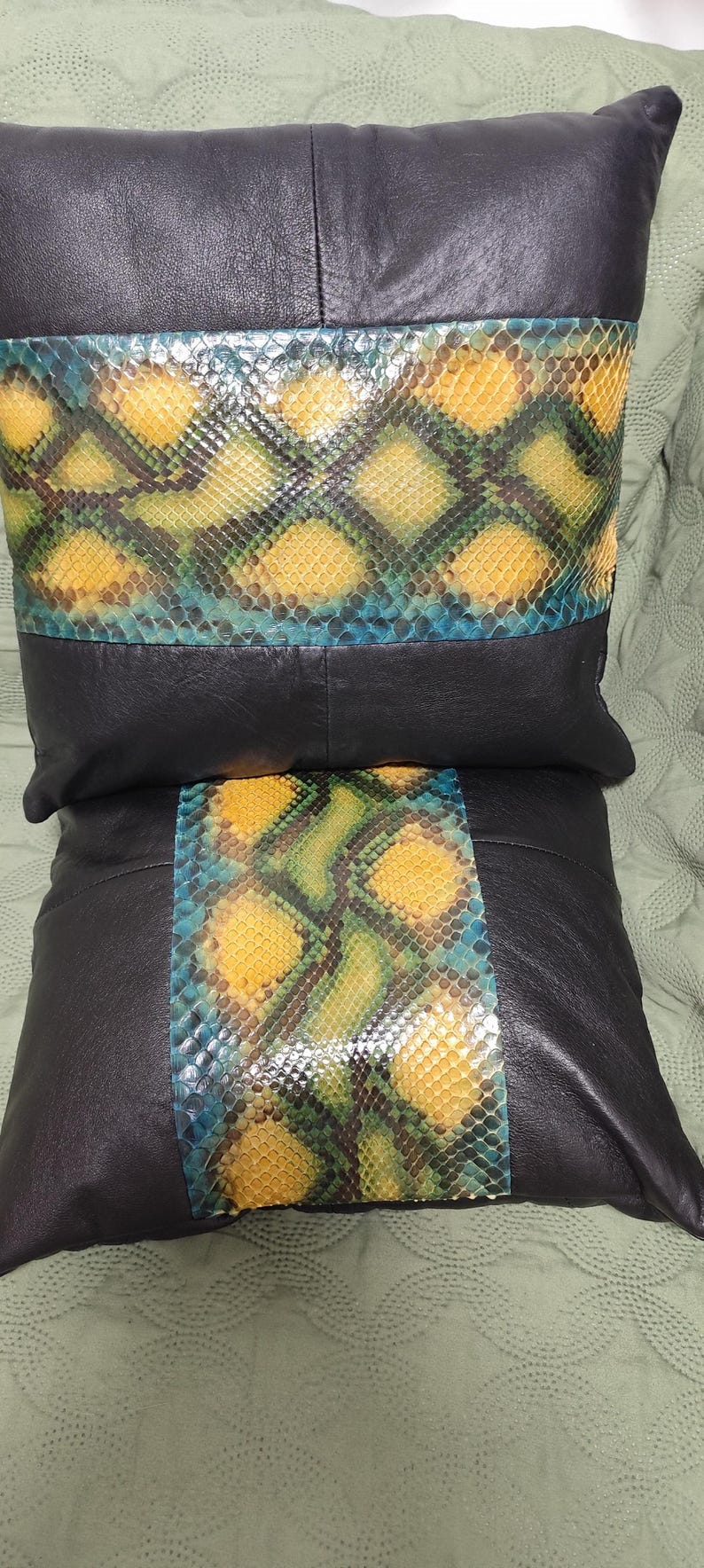 Op de afbeelding: Twee zwarte leren kussens met een geel, groen en blauw slangenhuidpatroon aan de voorkant.