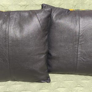 Op de afbeelding: Twee zwarte leren kussens met een subtiele glans. De kussens zijn rechthoekig en hebben een naad in het midden.