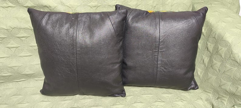 Op de afbeelding: Twee zwarte leren kussens met een subtiele glans. De kussens zijn rechthoekig en hebben een naad in het midden.