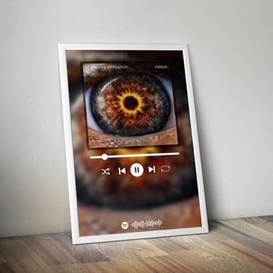 May include: A framed print featuring a close-up of a human eye with a brown iris and a black pupil. The print includes a music player interface with the text "breaking benjamin" and "EMBER". The eye is the focal point.