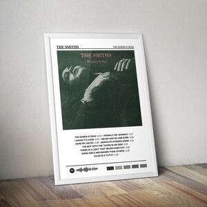 Peut inclure: Une affiche encadrée présentant la pochette de l'album "The Queen Is Dead" des Smiths. L'œuvre d'art est une image en noir et blanc d'une personne allongée. L'affiche comprend le nom du groupe et les titres des chansons.