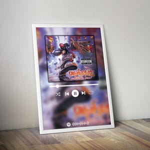 Puede incluir: Una impresión enmarcada en blanco de una pantalla de reproductor de música con un fondo borroso. La pantalla muestra una portada de álbum en blanco y negro con un gráfico de una persona con un atuendo rojo y azul. El título del álbum es "Significant Other" de "Ludacris". Los controles del reproductor de música son visibles en la parte inferior de la pantalla.