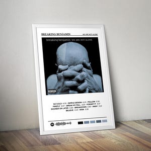 May include: A framed poster featuring the album art for "Breaking Benjamin We Are Not Alone." The image is a grayscale photo of a person with their hands clasped. The poster includes the album title, tracklist, and a Spotify code. The frame is white.