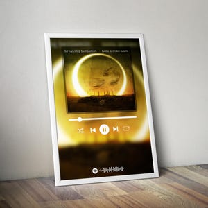 May include: A framed print featuring the album art for "Dark Before Dawn" by Breaking Benjamin. The artwork shows a yellow-orange ring with a dark landscape. A Spotify-style player interface is overlaid on the image.