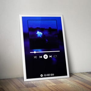 May include: A framed print with a dark blue gradient background. The print features a blurred image within a digital music player interface. The interface includes play, pause, skip, and rewind icons, along with a Spotify barcode at the bottom.