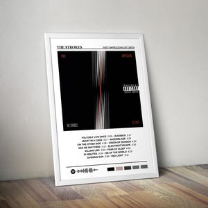 May include: A framed poster featuring the album art for "First Impressions of Earth" by The Strokes. The design has a black background with vertical white and orange lines. The tracklist and parental advisory are also visible.