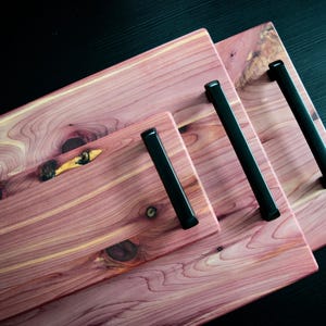 May include: Three wooden serving trays with black metal handles. The trays are made of cedar wood and are nested together.