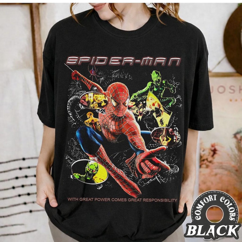 May include: Black t-shirt featuring a Spider-Man graphic. The design includes Spider-Man in a dynamic pose, the text "SPIDER-MAN", and the phrase "WITH GREAT POWER COMES GREAT RESPONSIBILITY". The shirt is a Comfort Colors brand.
