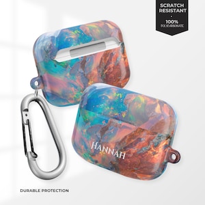 May include: Two AirPod cases with a colorful, marbled design in shades of blue, orange, and purple. One case has the name "HANNAH" printed on it. A silver carabiner clip is attached to one case. The text "SCRATCH RESISTANT" and "DURABLE PROTECTION" are visible.