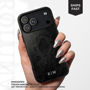May include: A black smartphone case featuring a textured snakeskin pattern and the initials K|M printed in white at the bottom. The case includes a circular MagSafe magnetic ring design on the back and a black camera module cutout area.