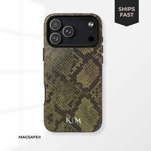 Könnte beinhalten: Eine grün-braune Handyhülle mit Schlangenmuster und schwarzem Kameramodul. Die Hülle hat die Initialen "K|M" in Weiß unten und das Wort "MAGSAFE®" unten links. Die Worte "SHIPS FAST" stehen in einem schwarzen Banner oben rechts.