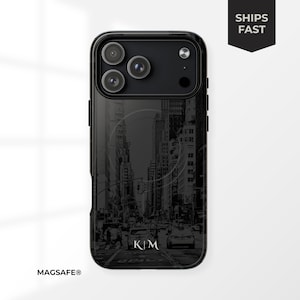 May include: Black phone case with a New York City street scene in grayscale. The case has a glossy finish and features the initials "KM" at the bottom. The words "MAGSAFE®" are printed at the bottom left and "SHIPS FAST" on the top right.