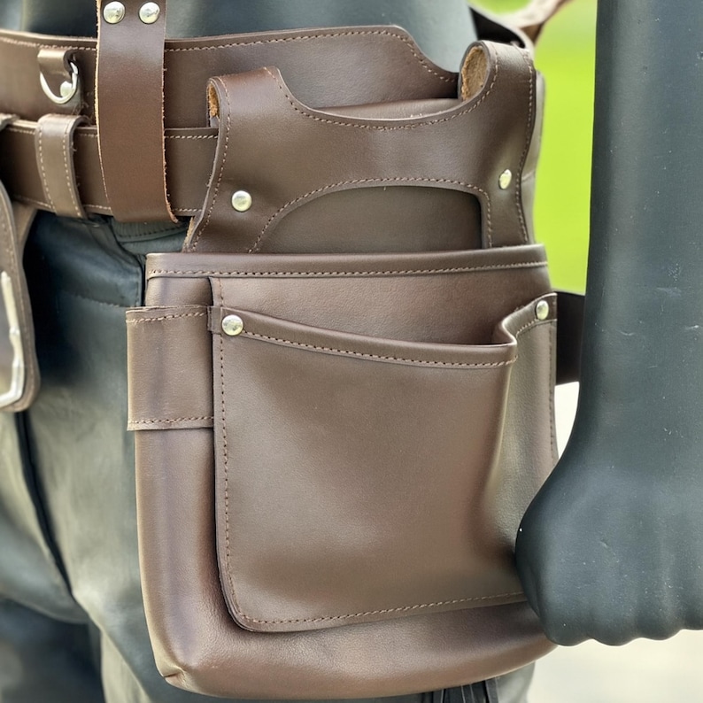 Close-up of right tool pouch in brown leather featuring dual pockets and riveted reinforcements.
