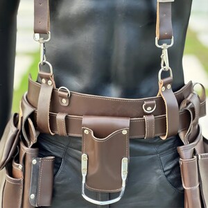 Close-up of leather work belt front section featuring D-rings, reinforced stitching, and hammer holder attachment.