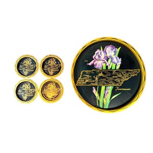 Puede incluir: Un juego de cuatro posavasos y una bandeja redonda. La bandeja presenta un fondo negro con un borde dorado, un mapa de Tennessee, iris moradas y la palabra "Tennessee". Los posavasos tienen un diseño dorado.