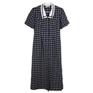 May include: A vintage midi dress with a black and white checkered pattern. The dress features a white collar with black trim, short sleeves, and a button-down front. The dress is hanging on a white hanger.