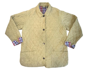 May include: A tan quilted jacket with a diamond pattern. The jacket has a collared neckline, three buttons, and two front pockets. The cuffs and inner collar feature a plaid pattern in red, blue, and purple.