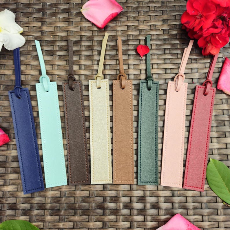 May include: A collection of seven leather bookmarks in various colors, including blue, mint green, brown, beige, tan, green, pink, and burgundy. Each bookmark has a matching loop and stitched edges.