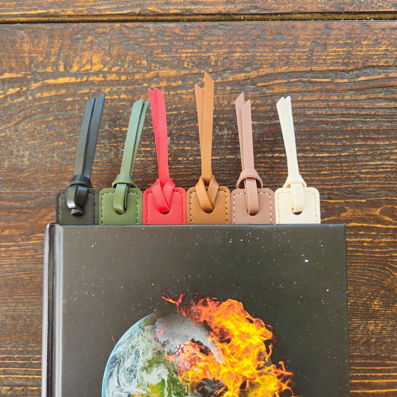 May include: A collection of leather bookmarks in various colors, including black, olive green, red, tan, light brown, and cream. Each bookmark is inserted into a book with a cover featuring an image of Earth engulfed in flames.