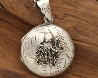 Könnte beinhalten: Silberne Halskette mit einem Anhänger in Form eines gravierten Oktopus. Der Anhänger ist rund und zeigt ein detailliertes Design eines Oktopus mit Tentakeln.