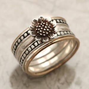 May include: A silver ring featuring a sunflower design. The ring is made up of multiple bands with a textured finish.