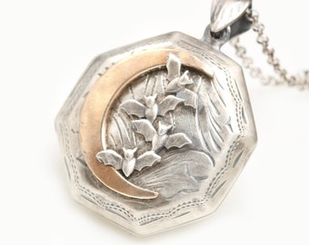 May include: A silver locket with a gold crescent moon and bats design. The locket is octagonal and has a detailed engraved pattern. It is attached to a silver chain.