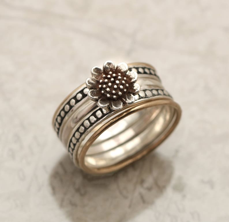 May include: A silver ring featuring a sunflower design. The ring is made up of multiple bands with a textured finish.