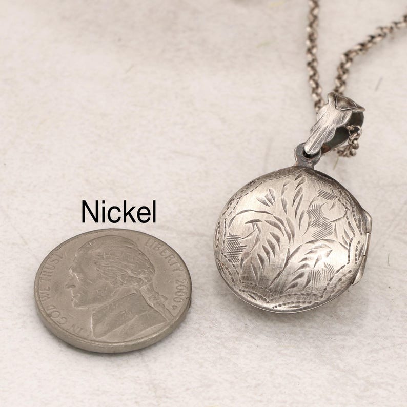 May include: A silver locket necklace with a floral design. The locket is about the size of a US nickel.
