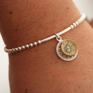 May include: A silver bracelet with a compass charm. The compass is round and has a gold face with black markings. The bracelet is made of small silver beads.