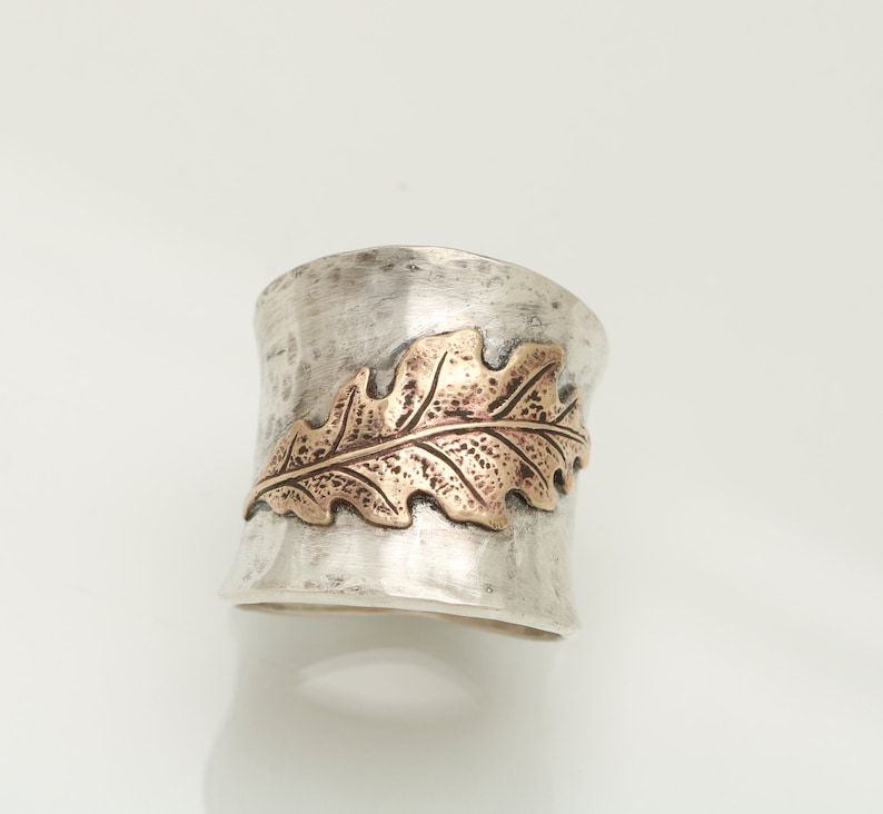 Puede incluir: Un anillo de plata con acabado martillado y un dise&ntilde;o de hoja de oro. La hoja es texturizada y tiene un patr&oacute;n de vetas detallado.