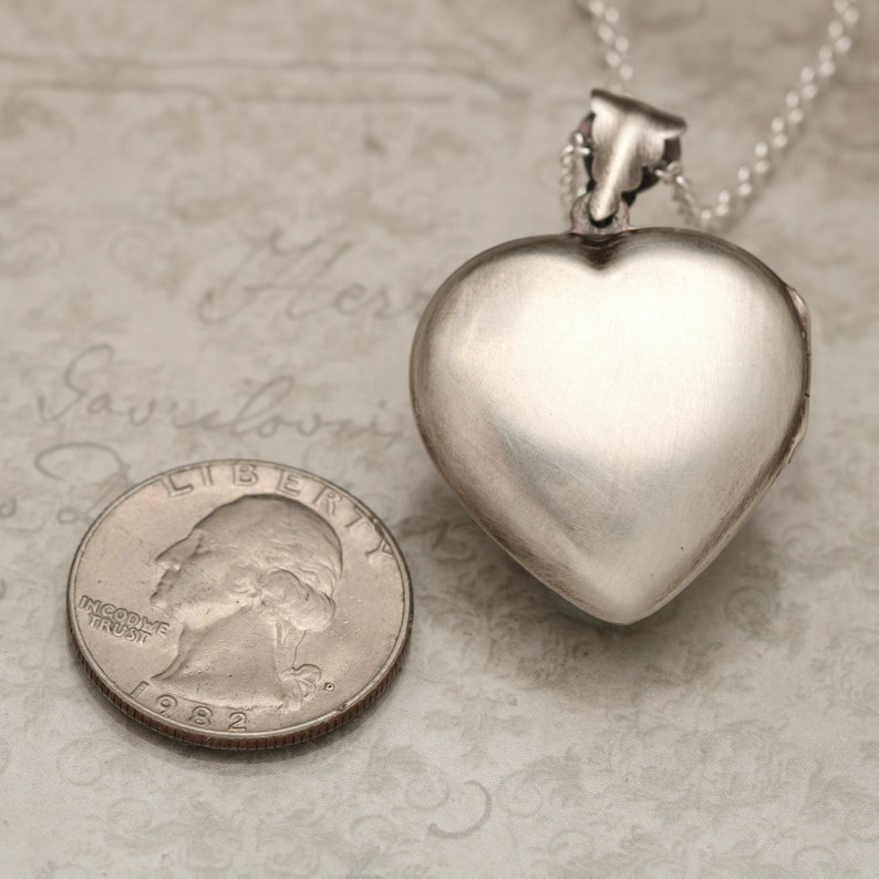 May include: Silver heart-shaped locket pendant with a chain. The locket is closed and has a smooth, polished surface.