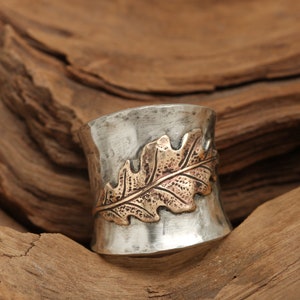 Puede incluir: Un anillo de plata con acabado martillado y un dise&ntilde;o de hoja de oro. El anillo es ancho y tiene una forma redondeada.