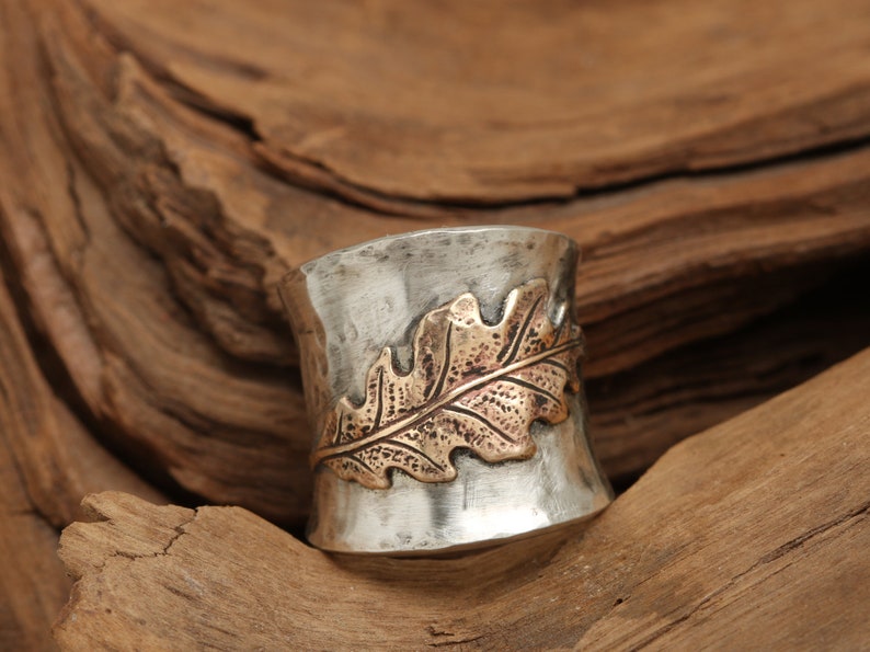 Puede incluir: Un anillo de plata con acabado martillado y un dise&ntilde;o de hoja de oro. El anillo es ancho y tiene una forma redondeada.