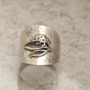 May include: A silver ring with a hammered texture features a detailed design of a ladybug on a leaf.