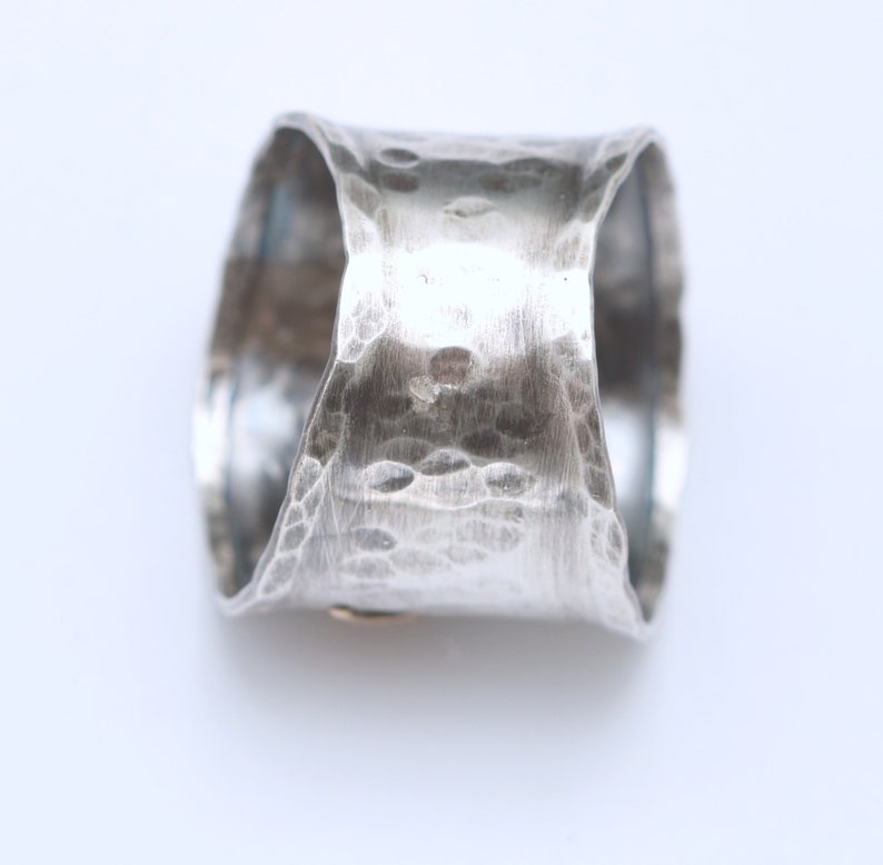 Puede incluir: Un anillo de plata con textura martillada. El anillo es ancho y tiene una forma redondeada.