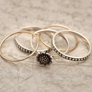 May include: A set of four silver rings, one with a textured pattern and another with a flower design. The rings are stacked on top of each other.