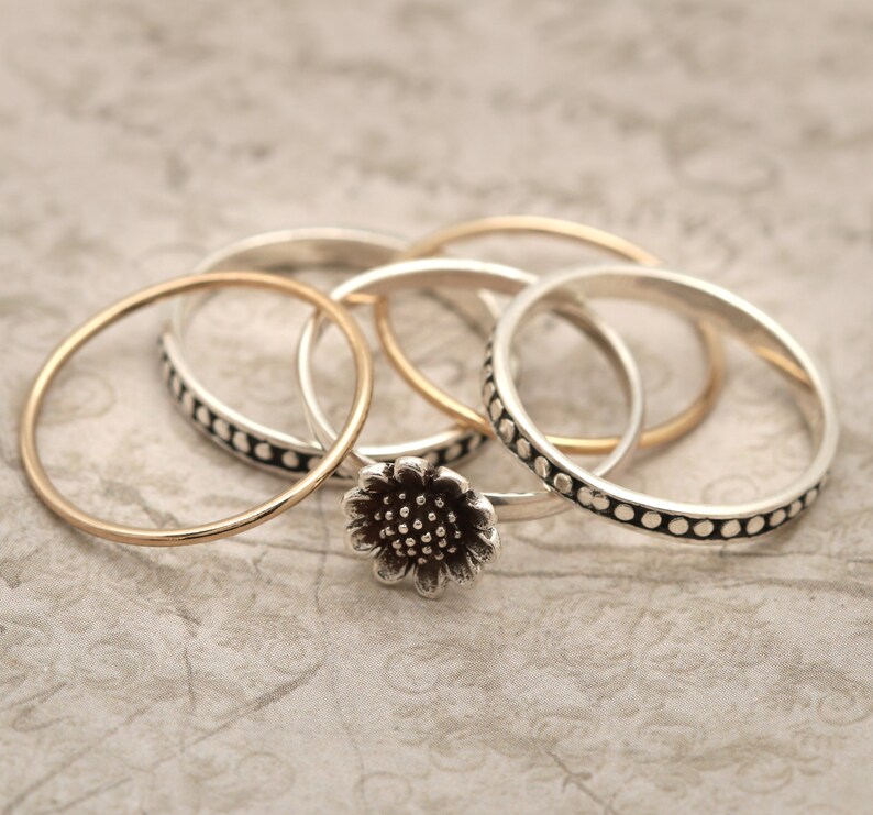 May include: A set of four silver rings, one with a textured pattern and another with a flower design. The rings are stacked on top of each other.