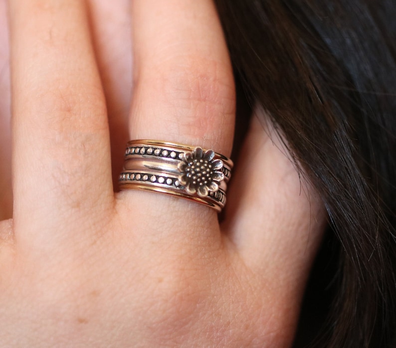 May include: A silver and gold ring with a sunflower design. The ring is made of multiple bands and has a textured finish.