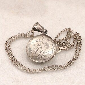 May include: A silver locket necklace with a delicate chain. The locket is round and features an engraved floral design.